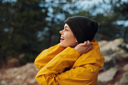 A woman in a yellow raincoat and beanie standing under the sky admiring the beauty of natureの写真素材