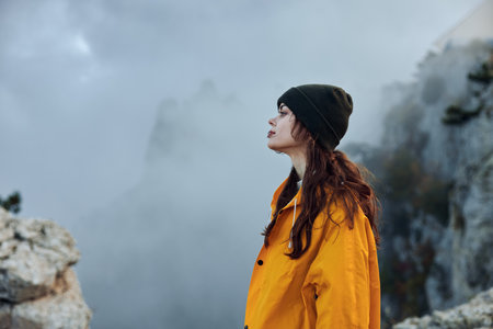 A woman in a yellow raincoat enjoying the majestic beauty of nature on a misty mountain top tripの写真素材