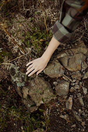 A hand reaching over a rock in the midst of a vast field under the open skyの写真素材