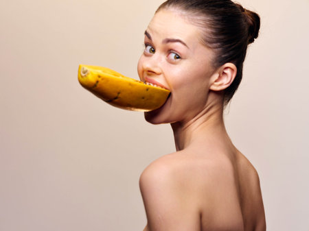Woman eating banana in playful and surreal fashion against neutral beige backgroundの写真素材