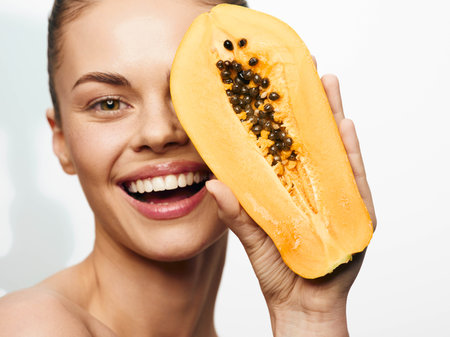 Smiling woman holding papaya in front of face, tropical fruit concept photo shoot with happy modelの写真素材
