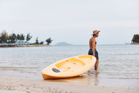Happy Asian Man Enjoying Kayaking Adventure on a Tropical Beachの写真素材