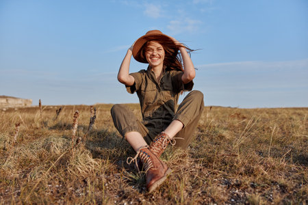 Happy woman relaxing in a serene field with a stylish hat, traveling in style and embracing natures beautyの写真素材