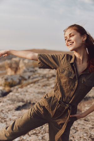 Woman in olive green jumpsuit standing on mountain top with arms outstretched in travel adventure beauty shotの写真素材