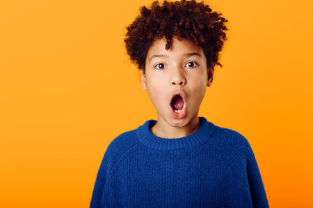 A surprised young african american boy with mouth wide open expressing excitement against a bright orange backgroundの写真素材