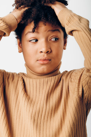 Young african american boy in a tan sweater sitting alone with his head in his hands, reflecting deep emotionsの写真素材