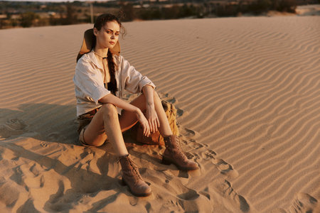 Desolate desert landscape with a woman sitting on top of a sand dune under the scorching sunの写真素材