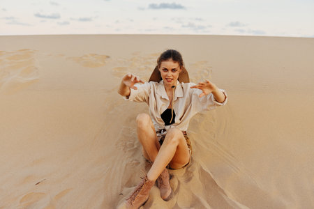 Woman sitting on top of sand dune with hands raised in air, enjoying peaceful and serene moment in desert wildernessの写真素材