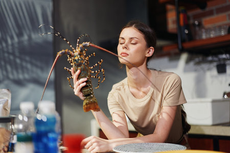 Woman holding a lobster at kitchen table Charming scene of female chef preparing seafood mealの写真素材