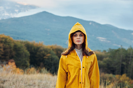 Woman in a yellow raincoat admiring the majestic mountains in a tranquil field during her peaceful travel journeyの写真素材