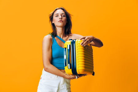Vibrant and bold woman embracing adventure with yellow suitcase against bright orange skyの写真素材