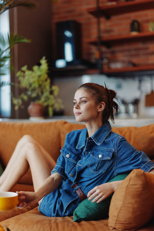 A woman relaxing on a couch with a cup of coffee and a plant in the backgroundの写真素材
