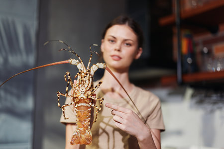 Woman Holding Lobster in Hand Standing in Front of Kitchen Counter, Food Preparation Conceptの写真素材