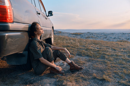 Traveling businesswoman resting next to car in the field during a road trip adventureの写真素材