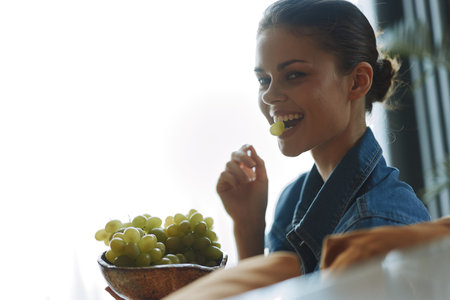 Woman enjoying a healthy snack of grapes while sitting at a table in a relaxing settingの写真素材