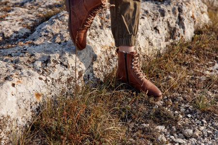 Person wearing brown boots standing on stone wall in field during travel adventure exploration trip...