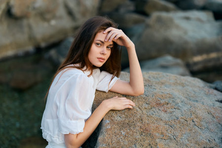 Serene young woman on coastal rock, contemplating the sea with elegance and graceの写真素材