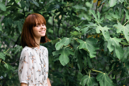 Vibrant redhead woman posing in lush green park setting with trees and leaves