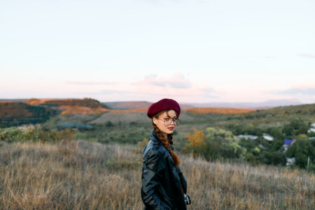 Stylish woman in red beret and leather jacket standing confidently in an open field