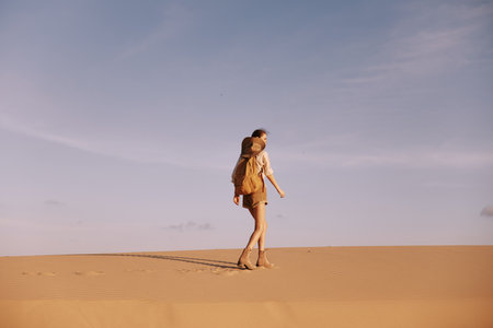 Lonely Wanderer A Woman Walking on Top of a Vast Sand Dune in the Desert Wildernessの写真素材