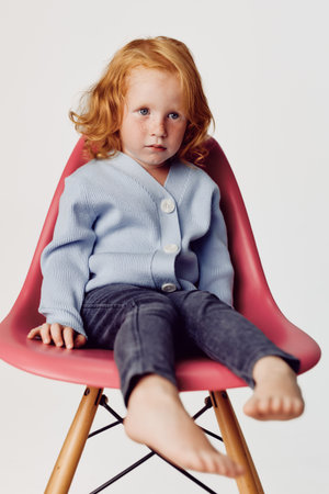 Redhaired girl sitting on pink chair in front of white background in a fashionable pose