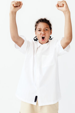 Excited young boy in white shirt and khaki pants raising arms in celebration on a sunny day