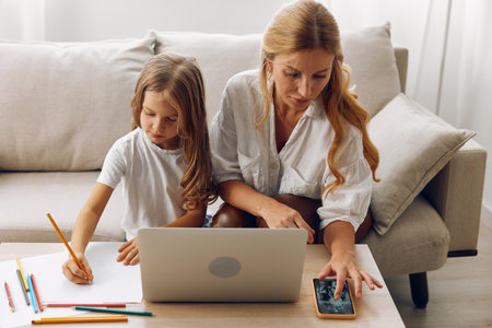 Woman and child sitting on couch using laptop and pencils for creative learning activitiesの写真素材