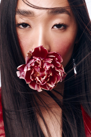 Beautiful woman with long black hair blowing a flower out of her face in a gentle breezeの写真素材