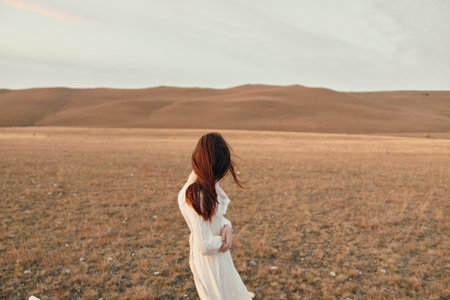 Serene woman in white dress standing in open field at sunset for travel and beauty concept
