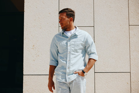 Young man in casual denim shirt standing against a modern concrete wall, looking away thoughtfully