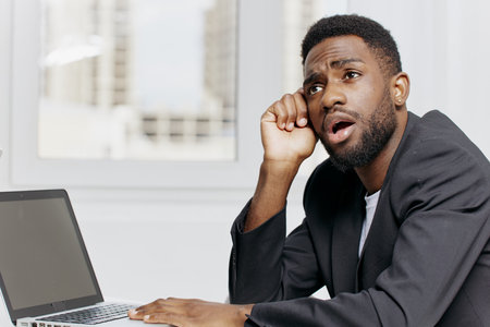 Businessman in deep thought working on a laptop, contemplating strategies and solutions at his office deskの写真素材