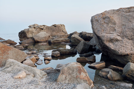 sunlit boulders lining the tranquil shores of a peaceful lake under the midday sunの写真素材