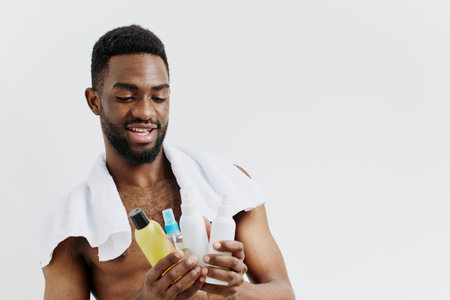 Shirtless man displaying skincare routine essentials with a bottle of lotion and tube of toothpaste in handの写真素材