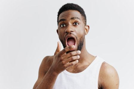 Surprised african american man with wide eyes and open mouth expressing shock and amazement on white backgroundの写真素材