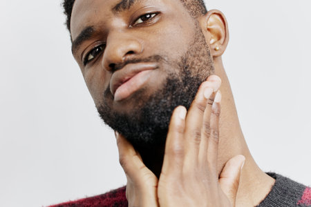 Pensive african american man in red sweater reflecting with hand on face in thoughtful momentの写真素材