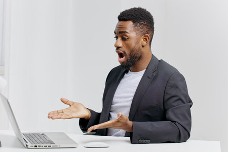 Surprised businessman reacts to shocking news on laptop while sitting at desk in professional office...