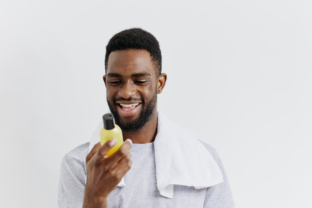 Confident young man showcasing beard care product with a bright smile against a clean white...