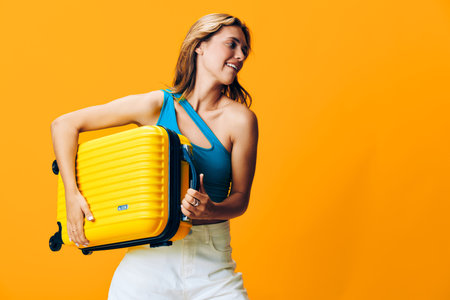 Happy traveler holding a vibrant yellow suitcase against a cheerful orange backdrop with a beaming smileの写真素材