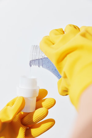 Woman in yellow gloves pouring hand sanitizer from bottle into another womans handの写真素材