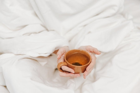 Person holding a coffee cup, lying on white bed with blanket and comforterの写真素材