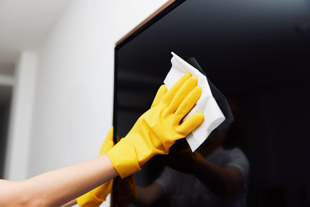 Cleaning a black television with yellow gloves