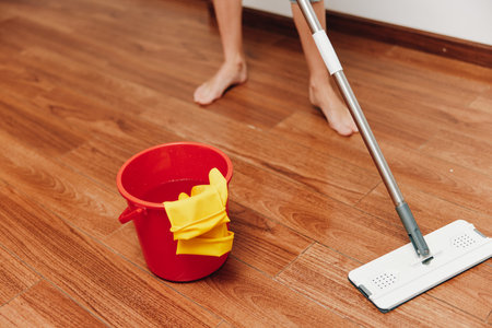 Woman cleaning wooden floor with mop and bucket of cleaning solution near red bucket and yellow ragの写真素材
