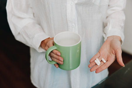 Woman holding a cup of coffee and a white pill in her hand, with another white pill in her other handの写真素材