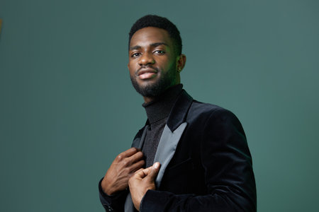 Stylish man in sleek black attire confidently poses against a vibrant green wall background