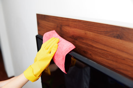 Woman in yellow gloves wiping down television on wooden shelf next to bookcaseの写真素材