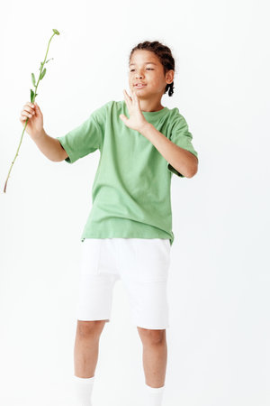 Young boy in green tshirt and white shorts holding a vibrant flower in a trendy poseの写真素材