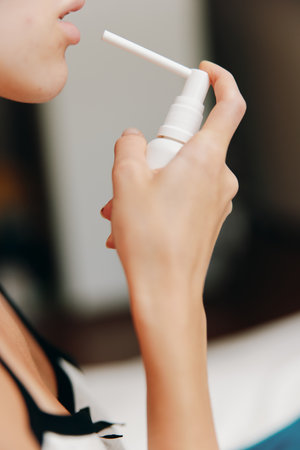 Woman sitting on bed in room with white background using air freshener on face