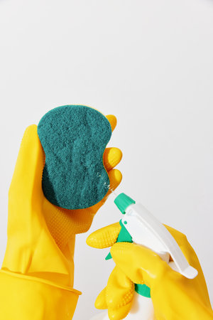 Woman in yellow gloves cleaning sponge with spray bottle on white background