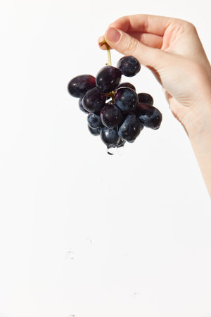 Person holding bunch of grapes over white surface with drop of water in middleの写真素材