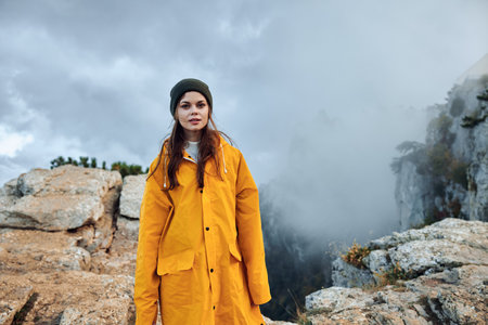 Young woman in a yellow raincoat standing on a misty mountain, embodying the beauty and tranquility...